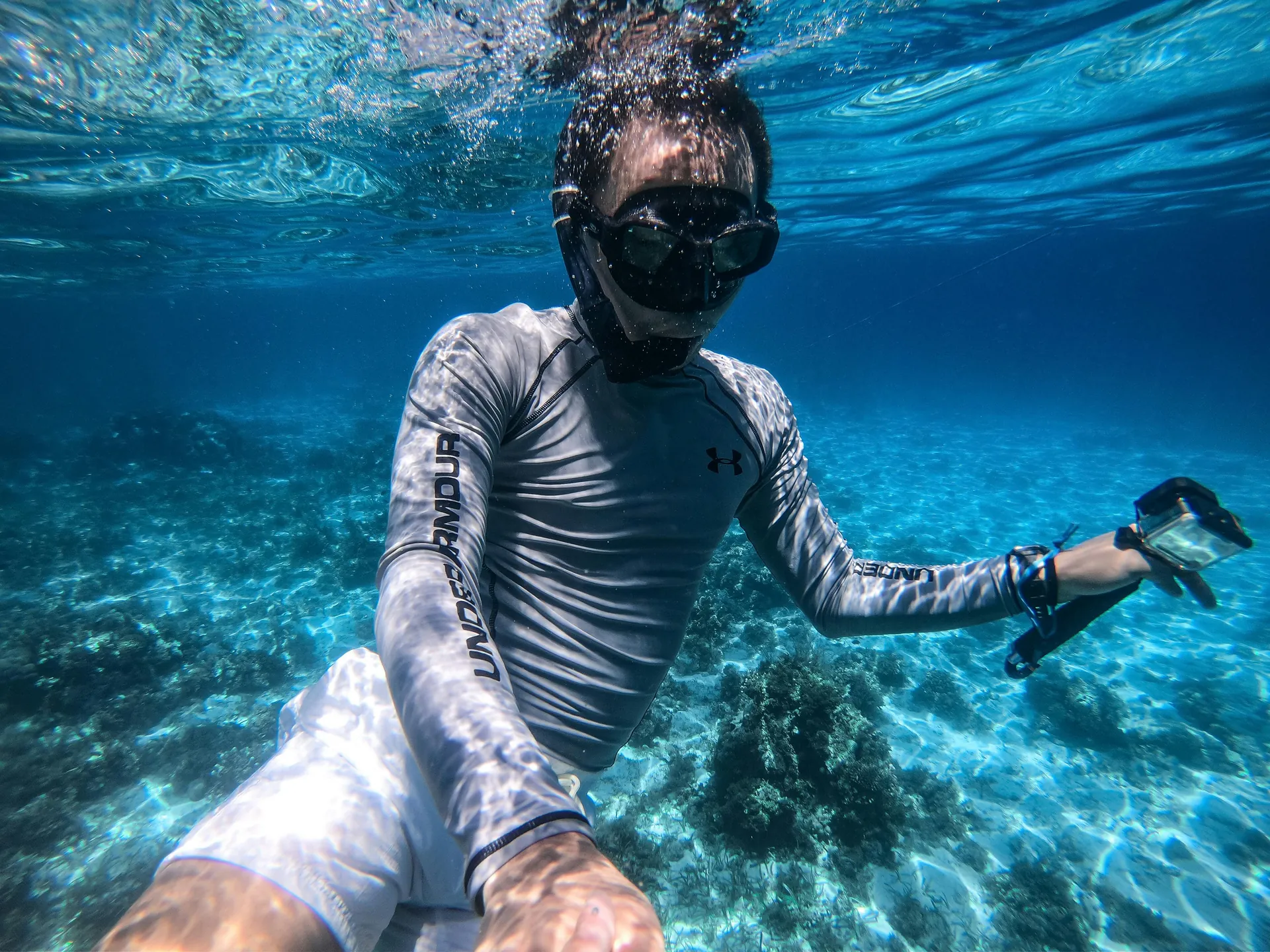 A man snorkeling in crystal clear blue ocean water, surrounded by coral, enjoying an underwater adventure.